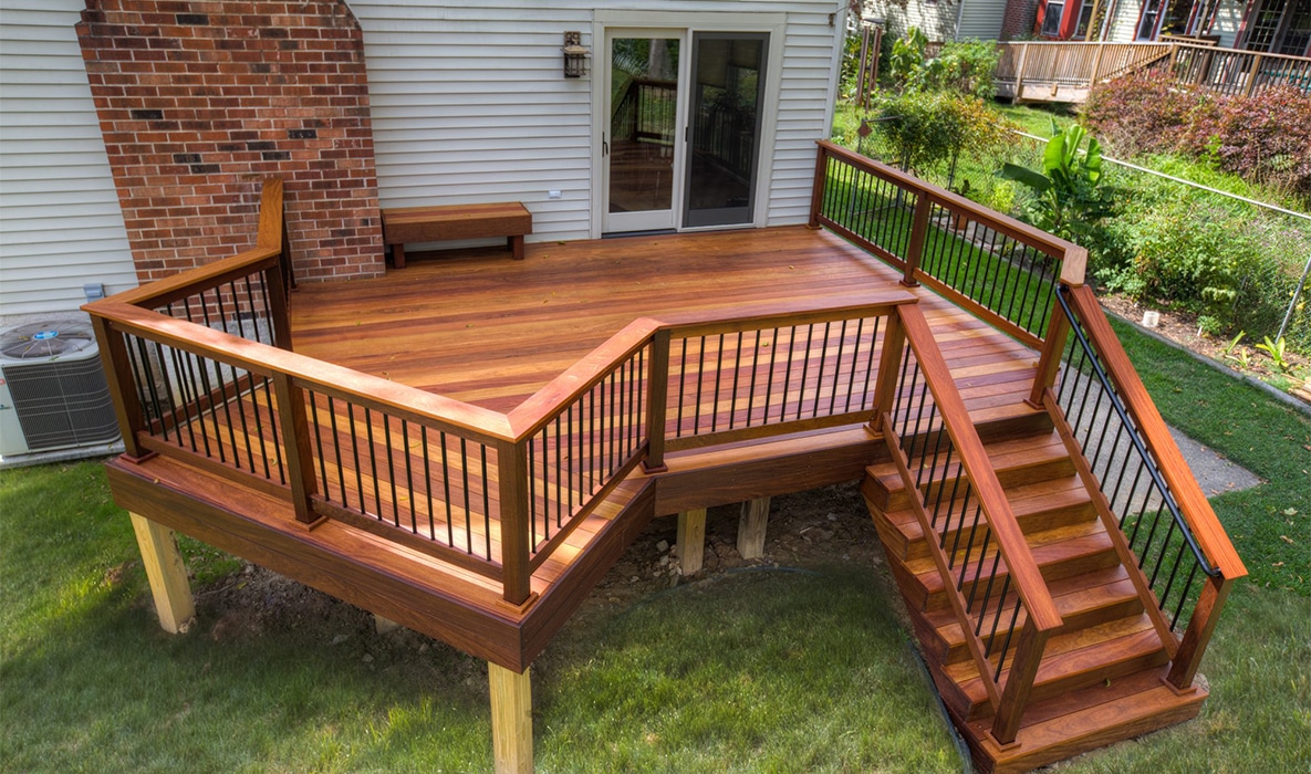 Photo of a raised wood deck with black railings and angled stairs in a backyard.